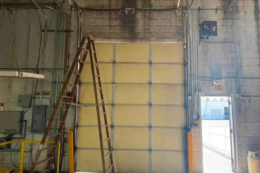 A tall sectional overhead door raised inside a block-walled service bay