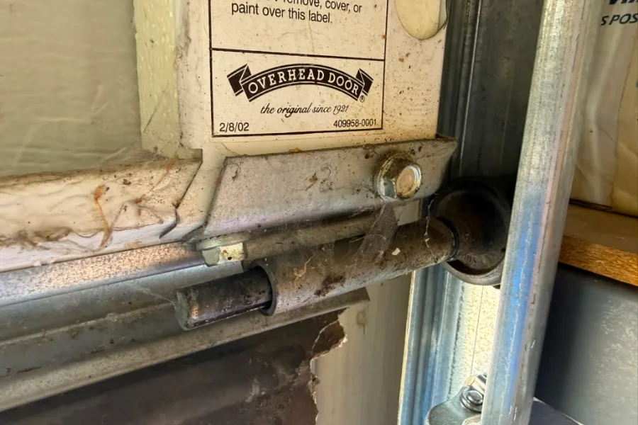 Worn garage door roller and hinge on a Gilbert door, with the 2002 manufacturer date label still visible