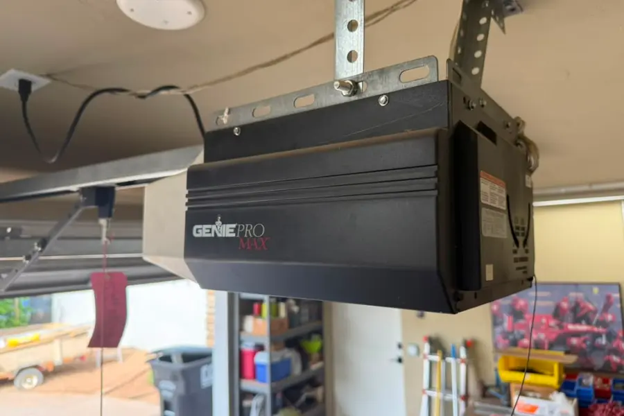 A garage door opener head unit fitted on its ceiling rail above stored items