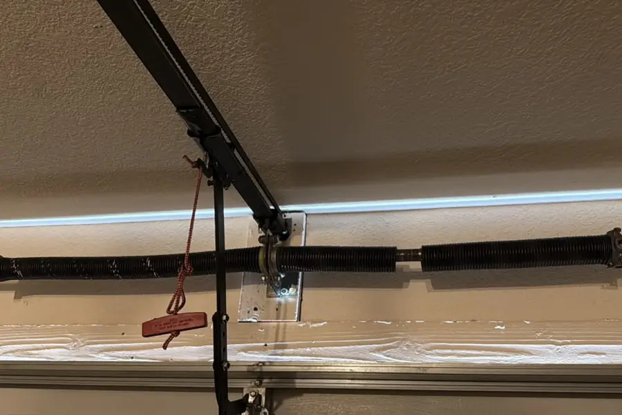 A replaced torsion spring on the shaft above a garage door with the release cord in view