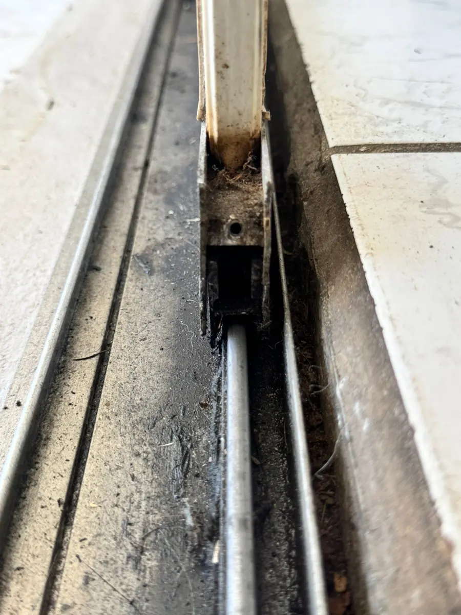 The bottom track of a sliding patio door packed with grit and worn along the rail